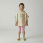 Ekru rengi lama nakışlı müslin panço giyen, pembe taytlı ve yeşil terlikli gülümseyen kız çocuk model.