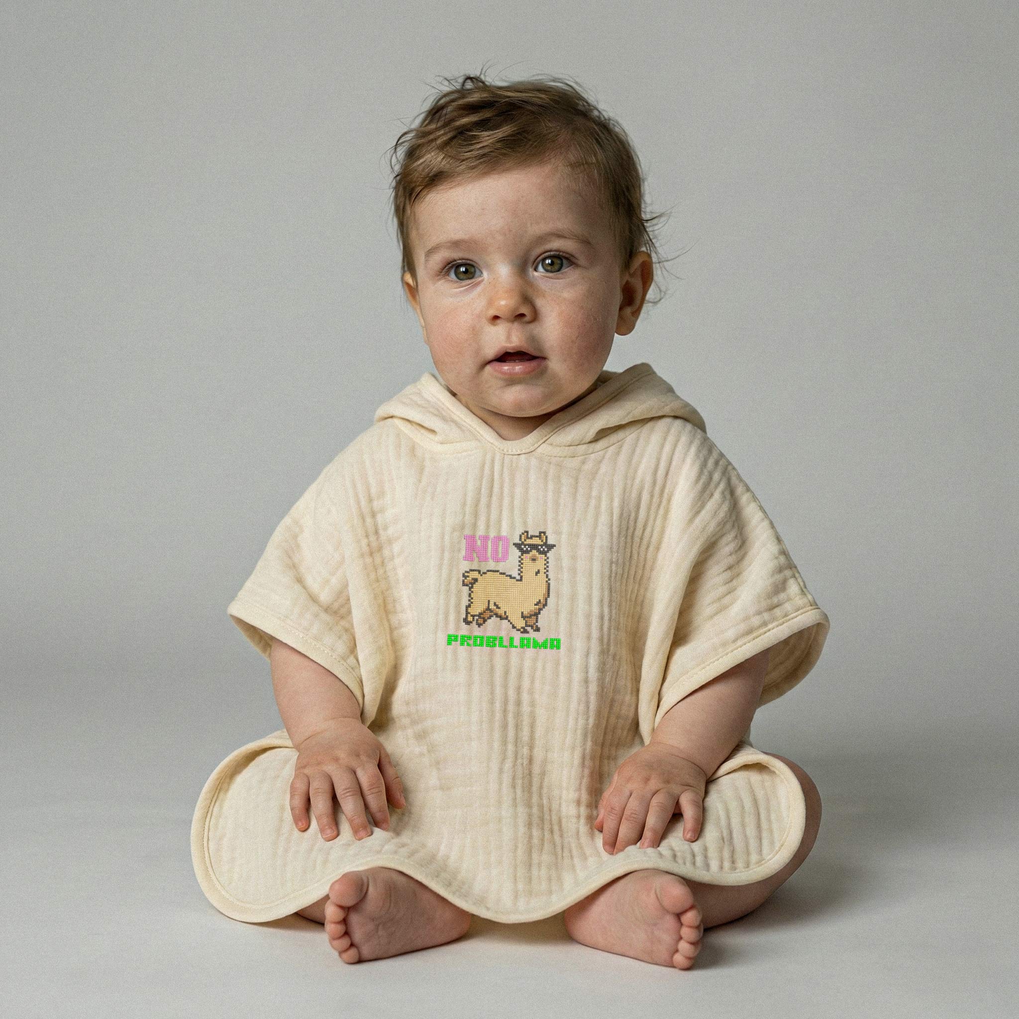 Doğal ekru renginde, üzerinde renkli lama nakışı bulunan kapüşonlu müslin panço giymiş erkek bebek model.