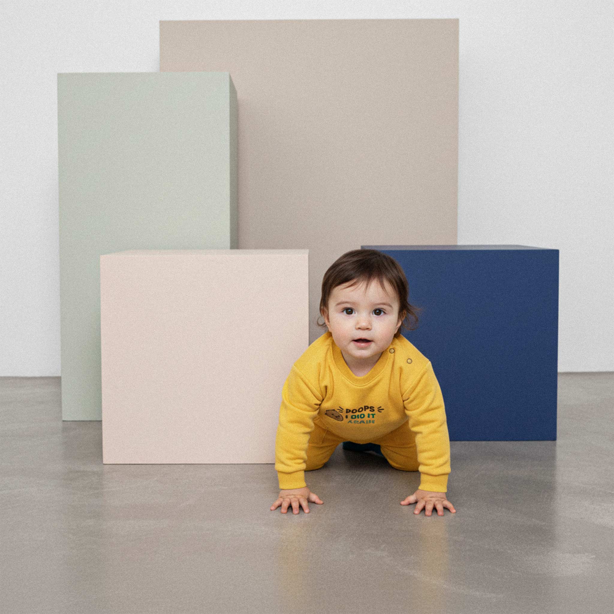 Üzerinde hardal sarısı renkli, 'Poops I Did It Again' nakışlı eşofman takımı bulunan sevimli bebek, renkli küplerin önünde emekleme pozisyonunda duruyor.