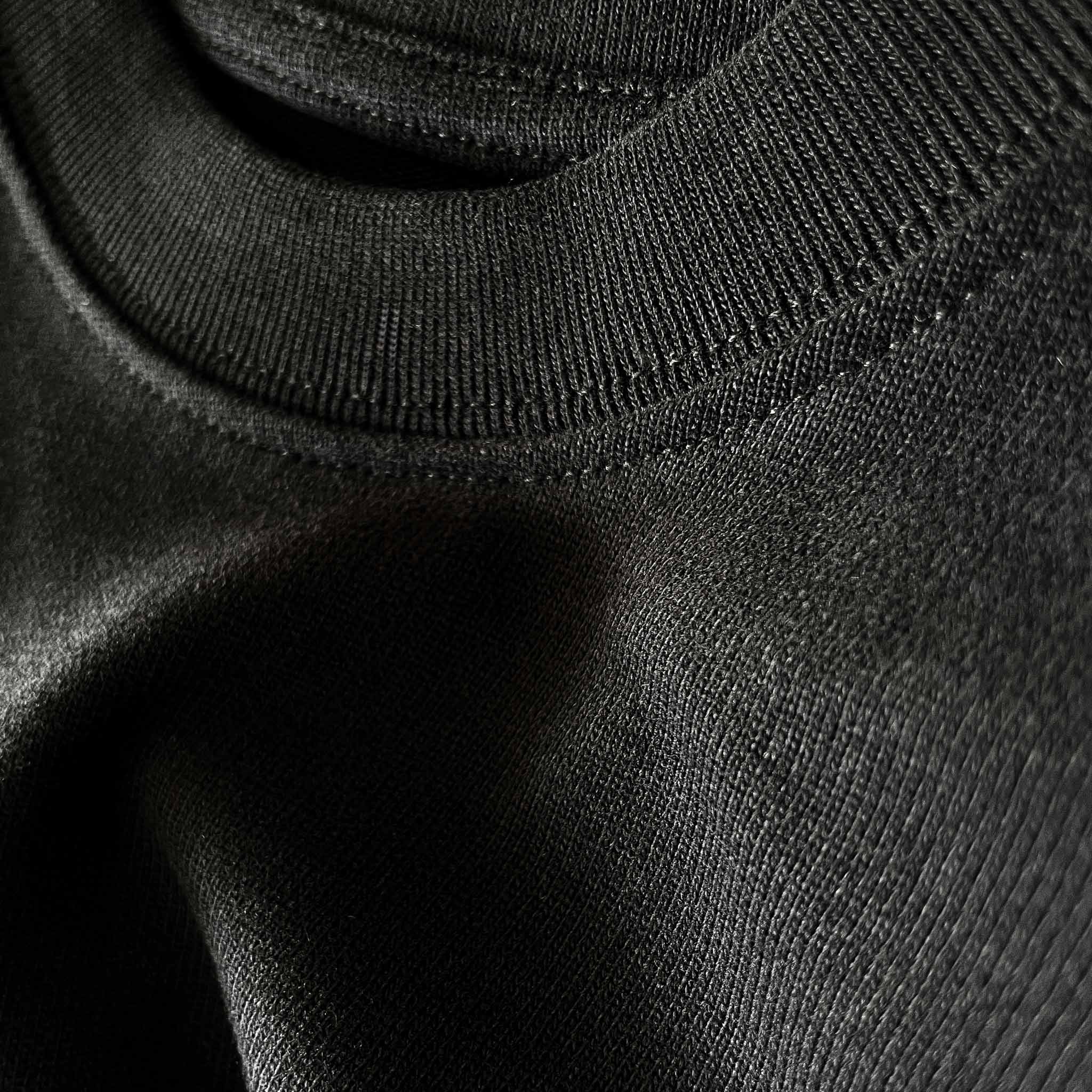 Siyah renkli premium oversize tişörtün dökümlü duruşunu, detay dikişlerini ve kalın fitilli yüksek esnek ribana yakasını sergileyen yakın plan fotoğraf.