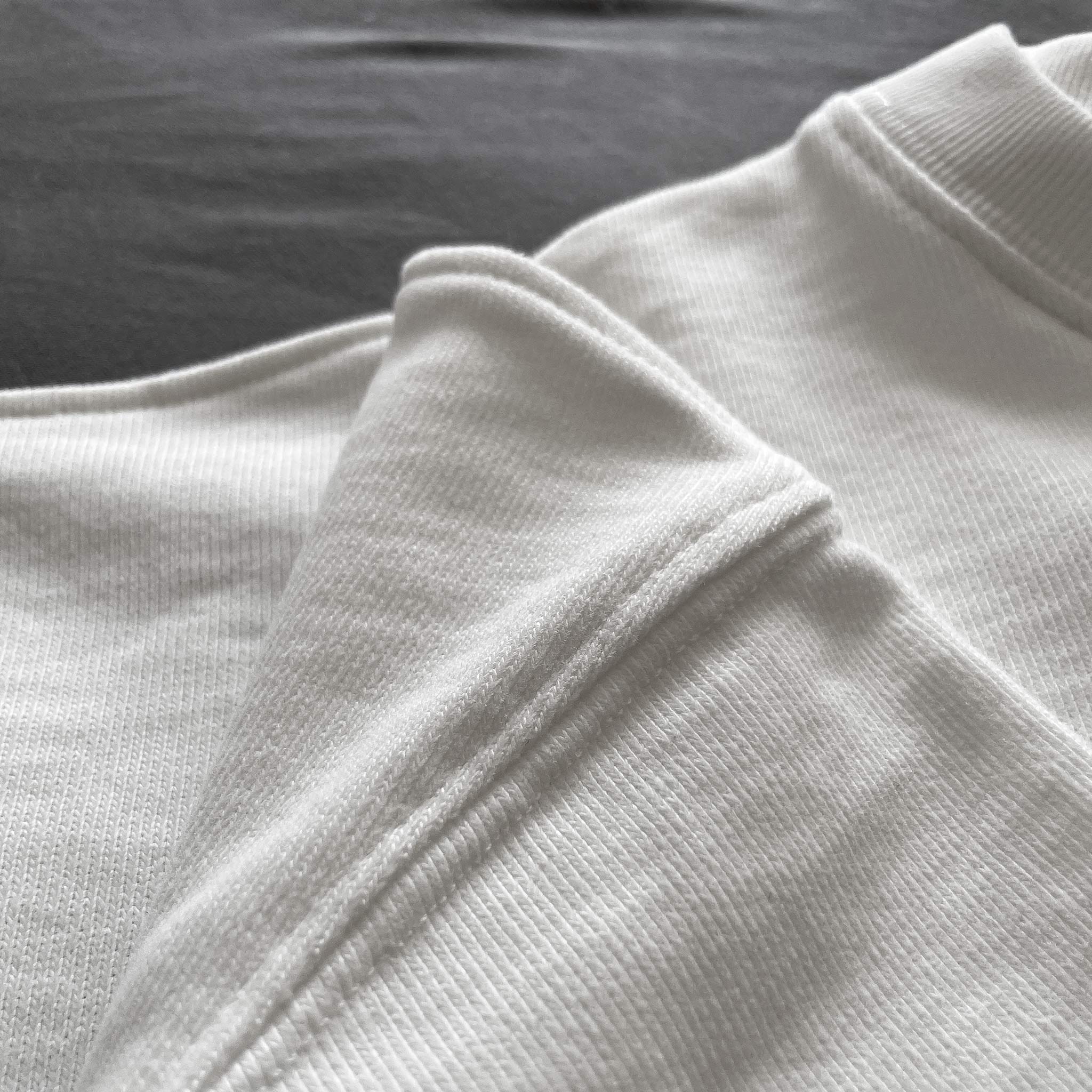 Ekru renkli premium oversize tişörtün katlanmış etek ucu kıvrımını, yüksek kalite dikiş işçiliğini ve %100 pamuklu tok kumaş dokusunu net bir şekilde gösteren yakın plan ürün fotoğrafı.