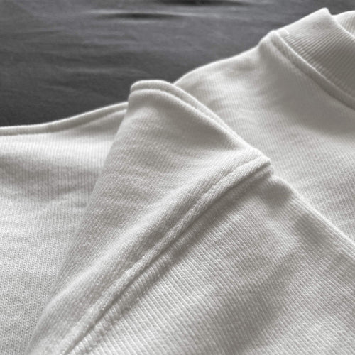 Ekru renkli premium oversize tişörtün katlanmış etek ucu kıvrımını, yüksek kalite dikiş işçiliğini ve %100 pamuklu tok kumaş dokusunu net bir şekilde gösteren yakın plan ürün fotoğrafı.