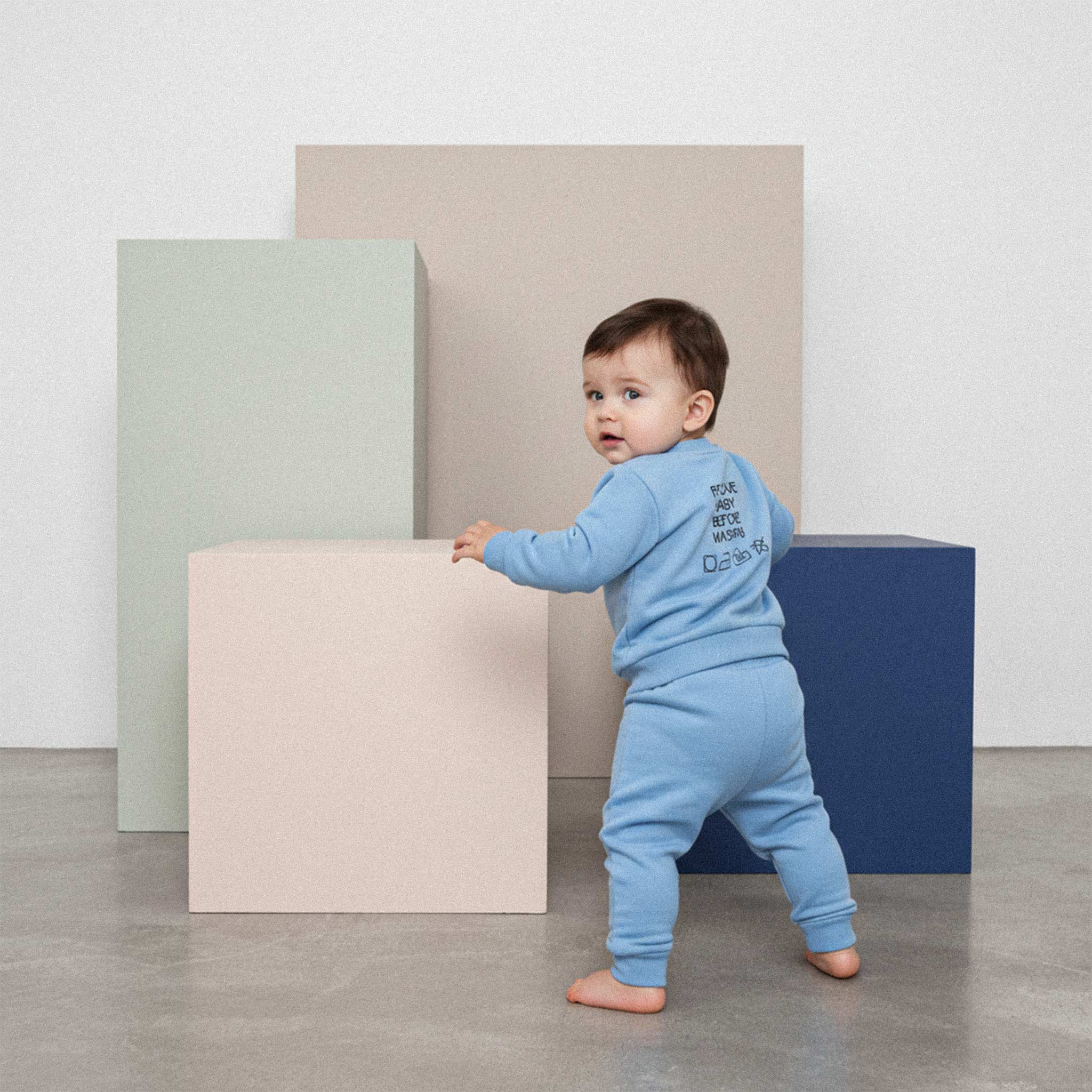 Üzerinde mavi renkli, 'Remove Baby Before Washing' nakışlı eşofman takımı bulunan sevimli bebek, renkli bir küpe tutunarak emekleme pozisyonunda duruyor.