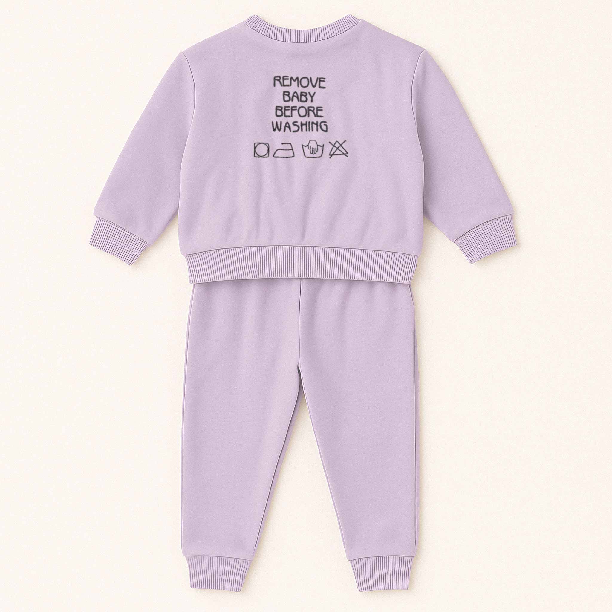 Lila (leylak) renkli, sweatshirt ve pantolondan oluşan pamuklu bebek eşofman takımı. Sweatshirt'ün arka tarafında "REMOVE BABY BEFORE WASHING" yazısı ve yıkama sembolleri işlenmiştir.