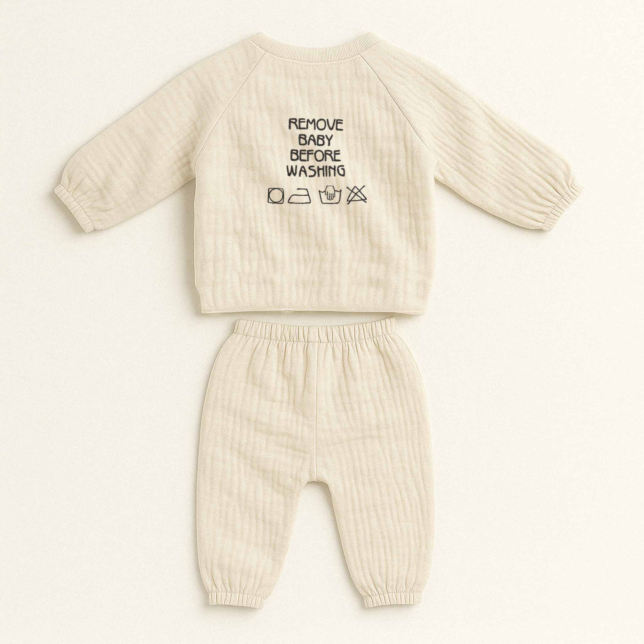 Doğal bej rengi müslin kimono takımının arka görünümü. Üst giyimin sırtında siyah iplikle "REMOVE BABY BEFORE WASHING" yazısı ve yıkama sembolleri işlenmiştir.