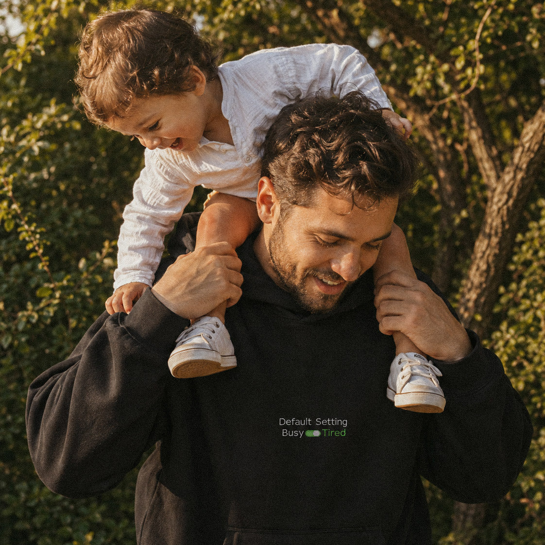 Çocuğunu omuzlarında taşıyan babanın doğada lifestyle çekimi. Babanın üzerinde esprili "Default Setting: Tired" nakışlı, siyah renkli kalın polar kapüşonlu sweatshirt. Konforlu ve premium Alman nakış işçiliği kışlık tasarım.