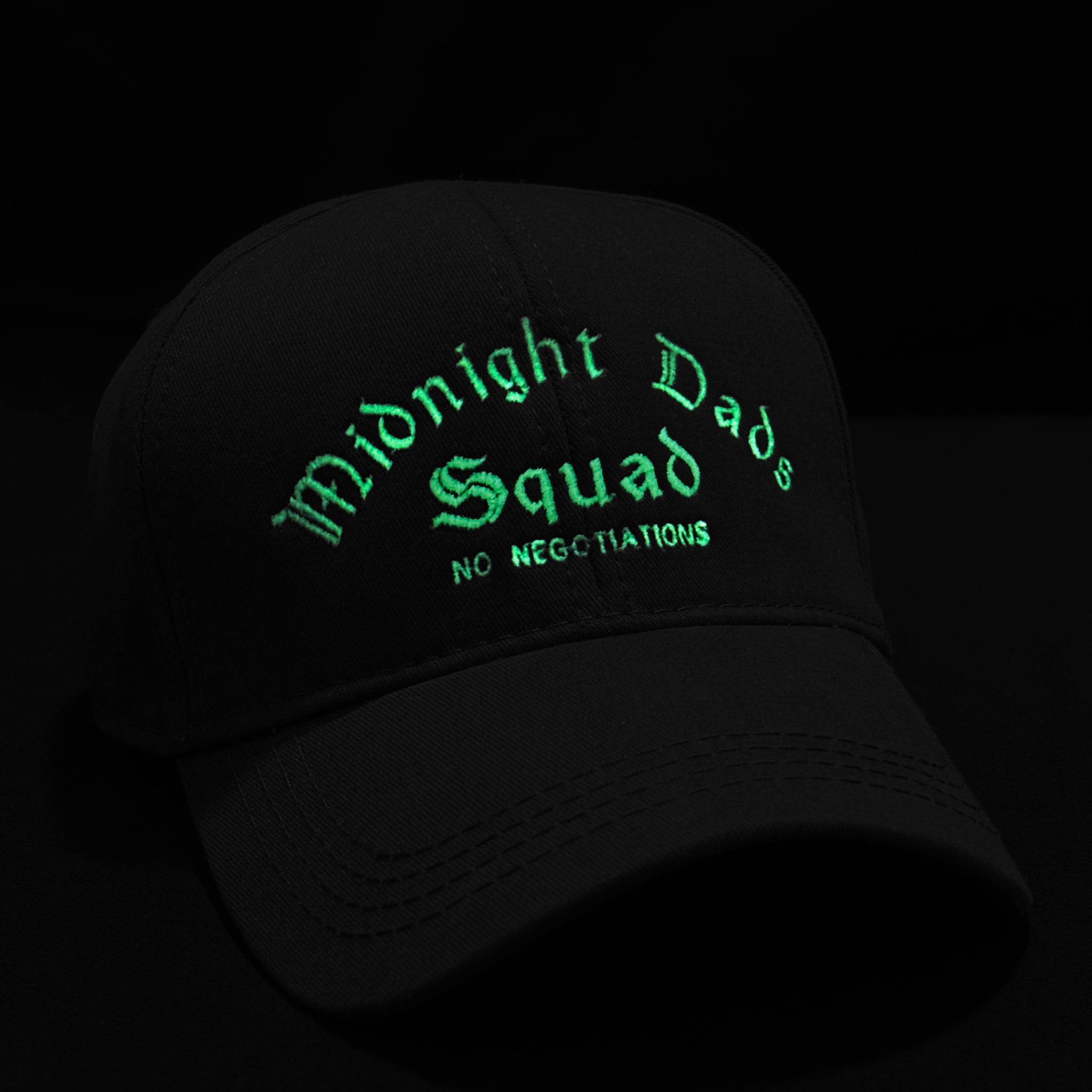 Şapka üzerine karanlıkta parlayan (glow-in-the-dark) özel iplikle işlenmiş nakışın gece görünümü. Gotik fontlu "Midnight Dads Squad" ve altındaki "NO NEGOTIATIONS" yazısı karanlıkta fosforlu yeşil bir ışık yayarak dikkat çekici ve iddialı bir stil sunar.