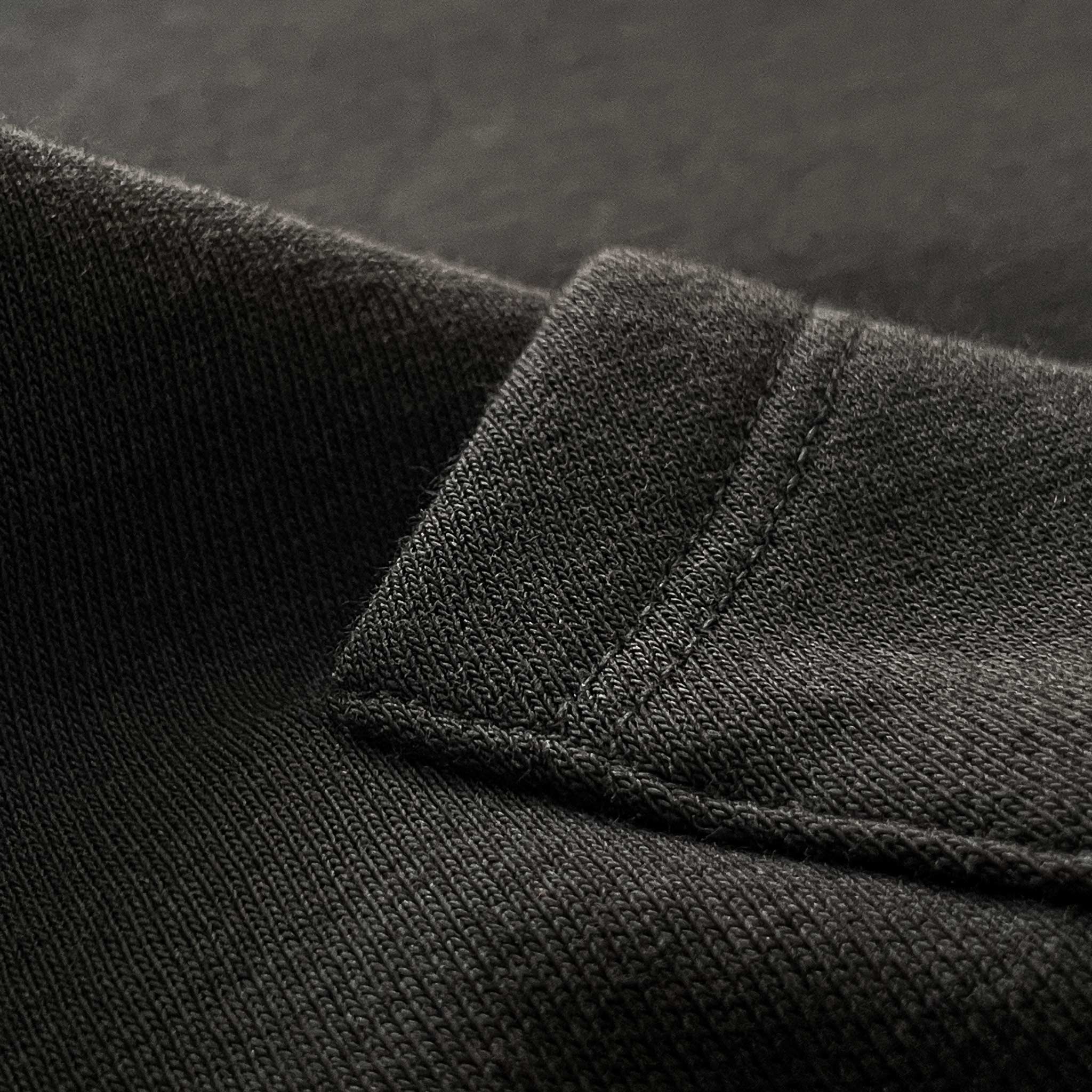 Siyah premium yetişkin pullover hoodie (kapüşonlu sweatshirt) modelinin kanguru cep yüzeyini ve tok pamuklu kumaş dokusunu gösteren makro detay çekimi. Ağır gramajlı (heavyweight) kumaşın yoğun örgüsü ve pürüzsüz yapısı ön plana çıkmaktadır. Kaliteli materyalin sunduğu dayanıklılık, şık döküm ve premium hissi vurgulayan yakın çekim.