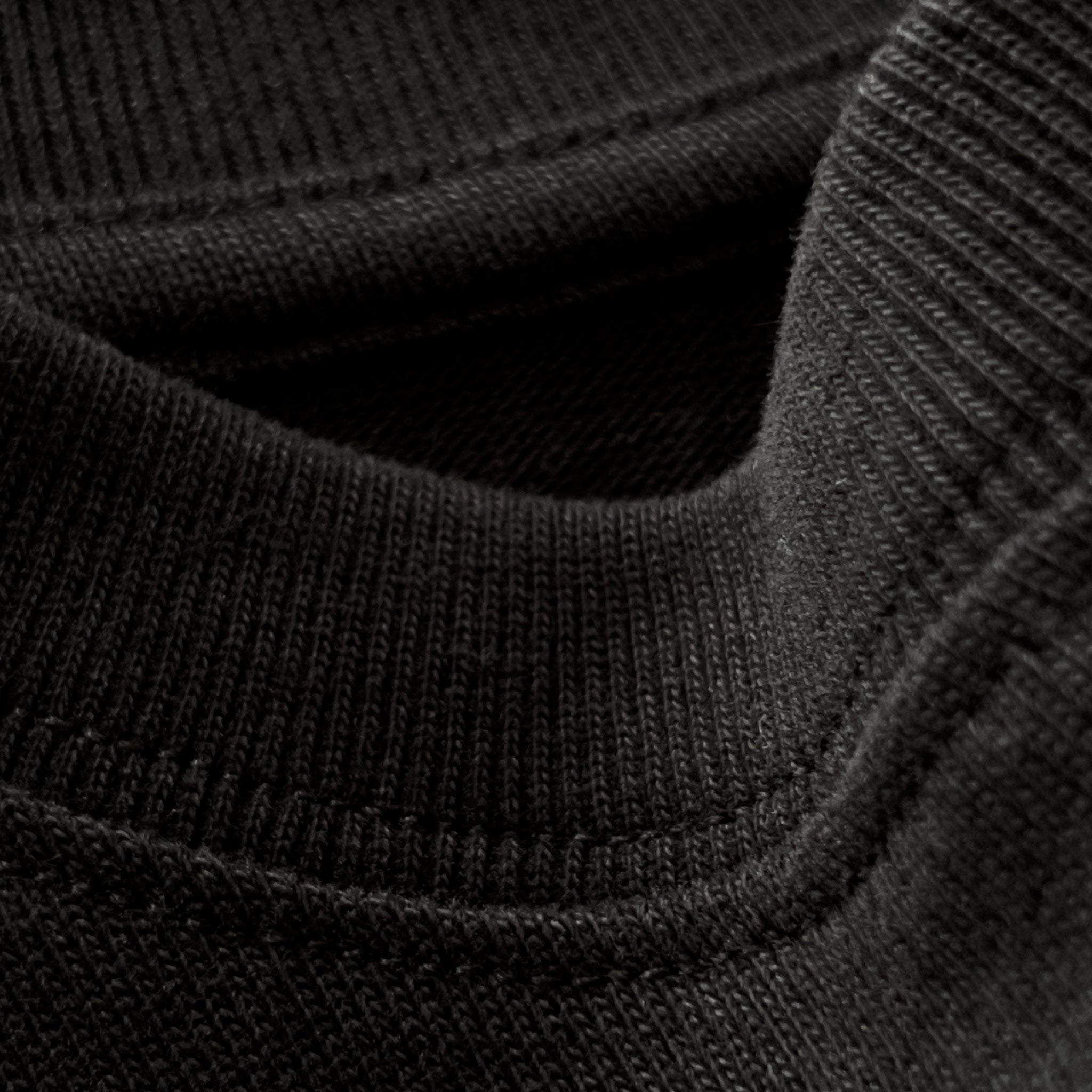 Siyah premium yetişkin t-shirt modelinin esnek fitilli yaka ribanasındaki dokuyu ve dikiş işçiliğini gösteren makro yakın çekim. Kaliteli ağır gramajlı pamuklu kumaşın yoğun örgüsü boynu nazikçe sararak konfor sunar ve formunu uzun süre bozmadan korur. Üstün konfor ve dayanıklılık vurgusu yapan yapısal detay.