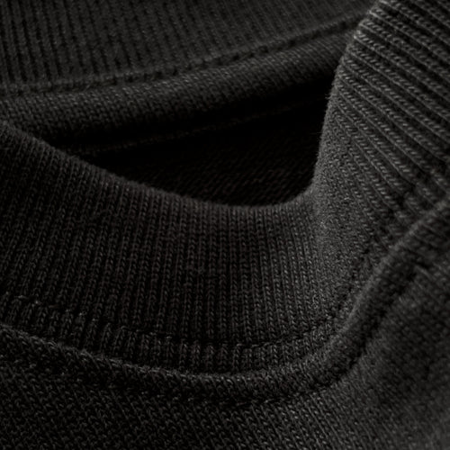 Siyah premium yetişkin t-shirt modelinin esnek fitilli yaka ribanasındaki dokuyu ve dikiş işçiliğini gösteren makro yakın çekim. Kaliteli ağır gramajlı pamuklu kumaşın yoğun örgüsü boynu nazikçe sararak konfor sunar ve formunu uzun süre bozmadan korur. Üstün konfor ve dayanıklılık vurgusu yapan yapısal detay.