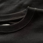 Siyah premium yetişkin t-shirt modelinin esnek fitilli yaka ribanasını ve tok pamuklu kumaş dokusunu gösteren yakın çekim. Kaliteli ağır gramajlı (heavyweight) kumaşın yoğun örgüsü boynu nazikçe sarar ve tok duruşuyla formunu korur. Minimalist şıklık ve premium konfor sunan yapısal detay.