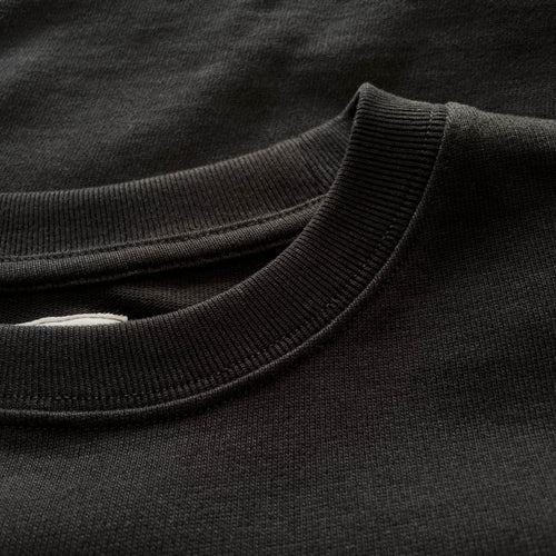 Siyah premium yetişkin t-shirt modelinin esnek fitilli yaka ribanasını ve tok pamuklu kumaş dokusunu gösteren yakın çekim. Kaliteli ağır gramajlı (heavyweight) kumaşın yoğun örgüsü boynu nazikçe sarar ve tok duruşuyla formunu korur. Minimalist şıklık ve premium konfor sunan yapısal detay.