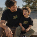 Siyah renkli "THE BEST DAD IN THE GALAXY" ve "THE BEST DUDE IN THE GALAXY" sarı ve yeşil iplik nakışlı baba-oğul kombin tişörtleri. %100 pamuklu, nefes alan Oeko-Tex sertifikalı heavyweight kumaştan üretilmiştir. Açık alanda keyifli anları yansıtan premium lifestyle baba-çocuk giyim çekimi.