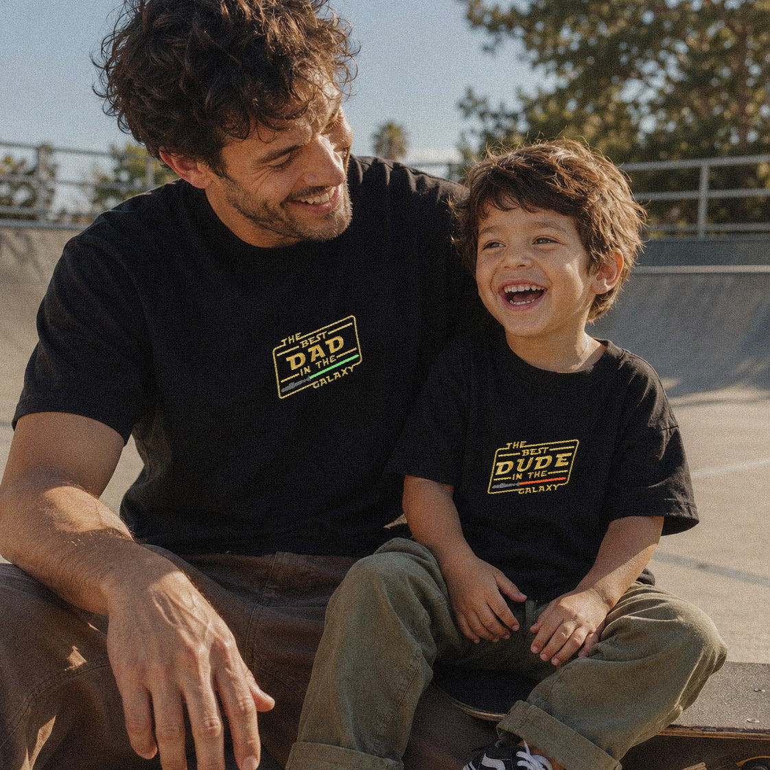 Siyah renkli "THE BEST DAD IN THE GALAXY" ve "THE BEST DUDE IN THE GALAXY" sarı ve yeşil iplik nakışlı baba-oğul kombin tişörtleri. %100 pamuklu, nefes alan Oeko-Tex sertifikalı heavyweight kumaştan üretilmiştir. Açık alanda keyifli anları yansıtan premium lifestyle baba-çocuk giyim çekimi.