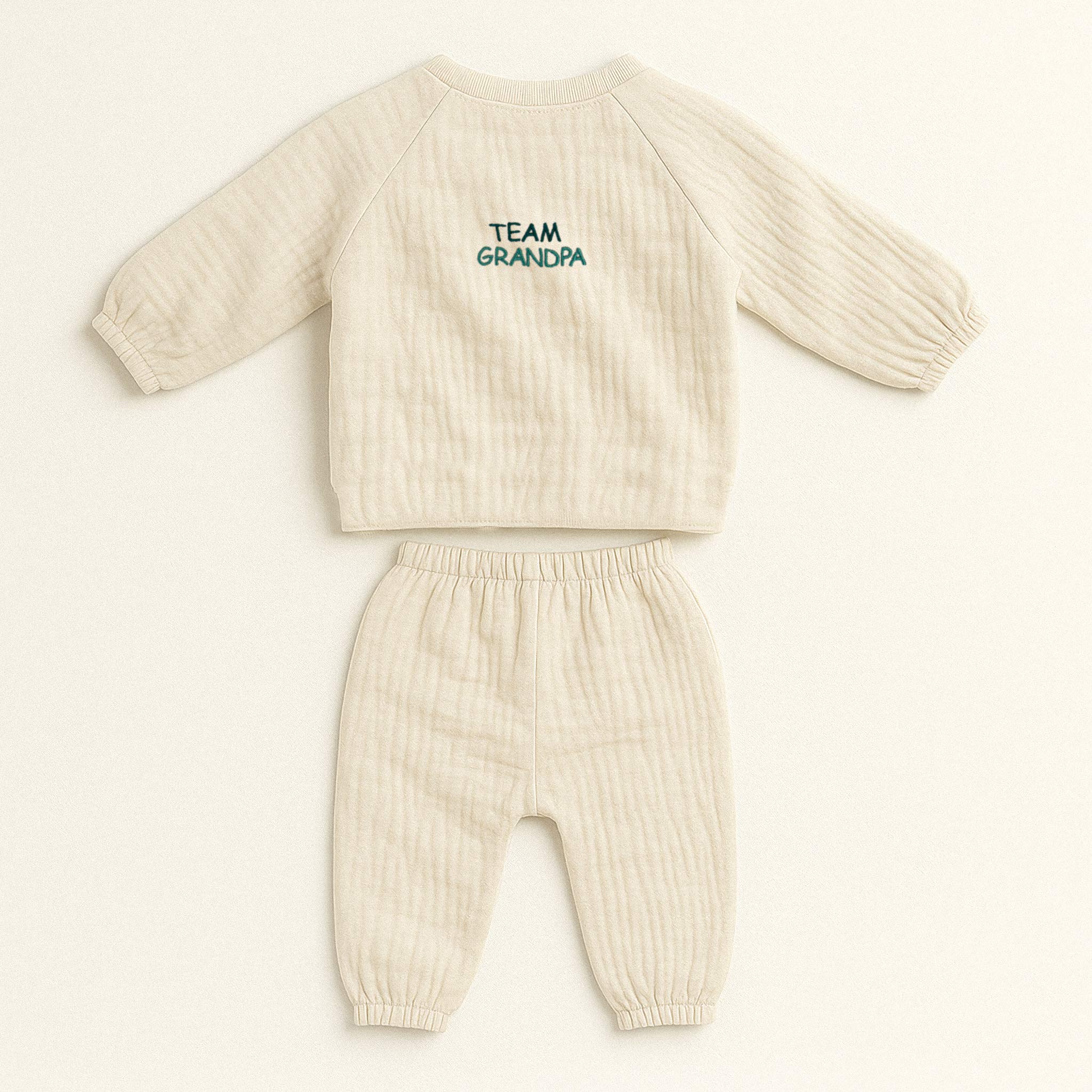 Doğal bej (ekru) renginde, müslin kumaştan yapılmış, üzerinde 'Team Grandpa' nakışı bulunan, yandan bağlamalı kimono üst ve pantolondan oluşan yenidoğan bebek takımı.