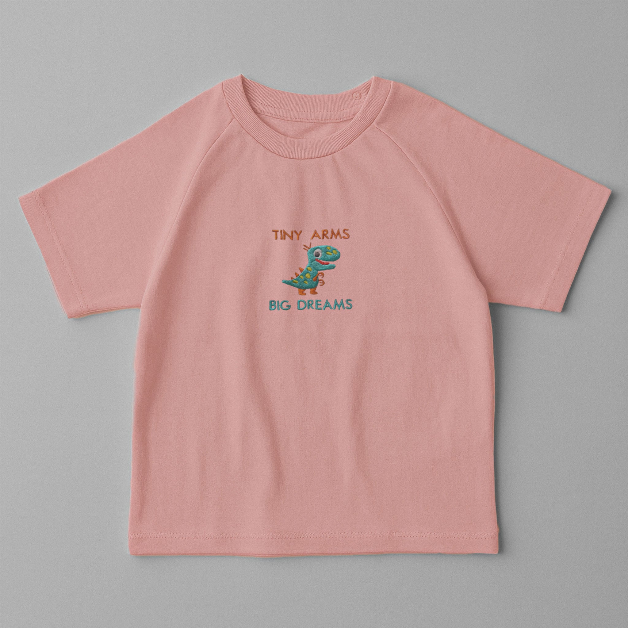 Gül kurusu (pembe) renkli, omuzdan çıtçıtlı, üzerinde sevimli dinozor nakışı ve 'Tiny Arms Big Dreams' yazısı bulunan pamuklu bebek tişörtü.