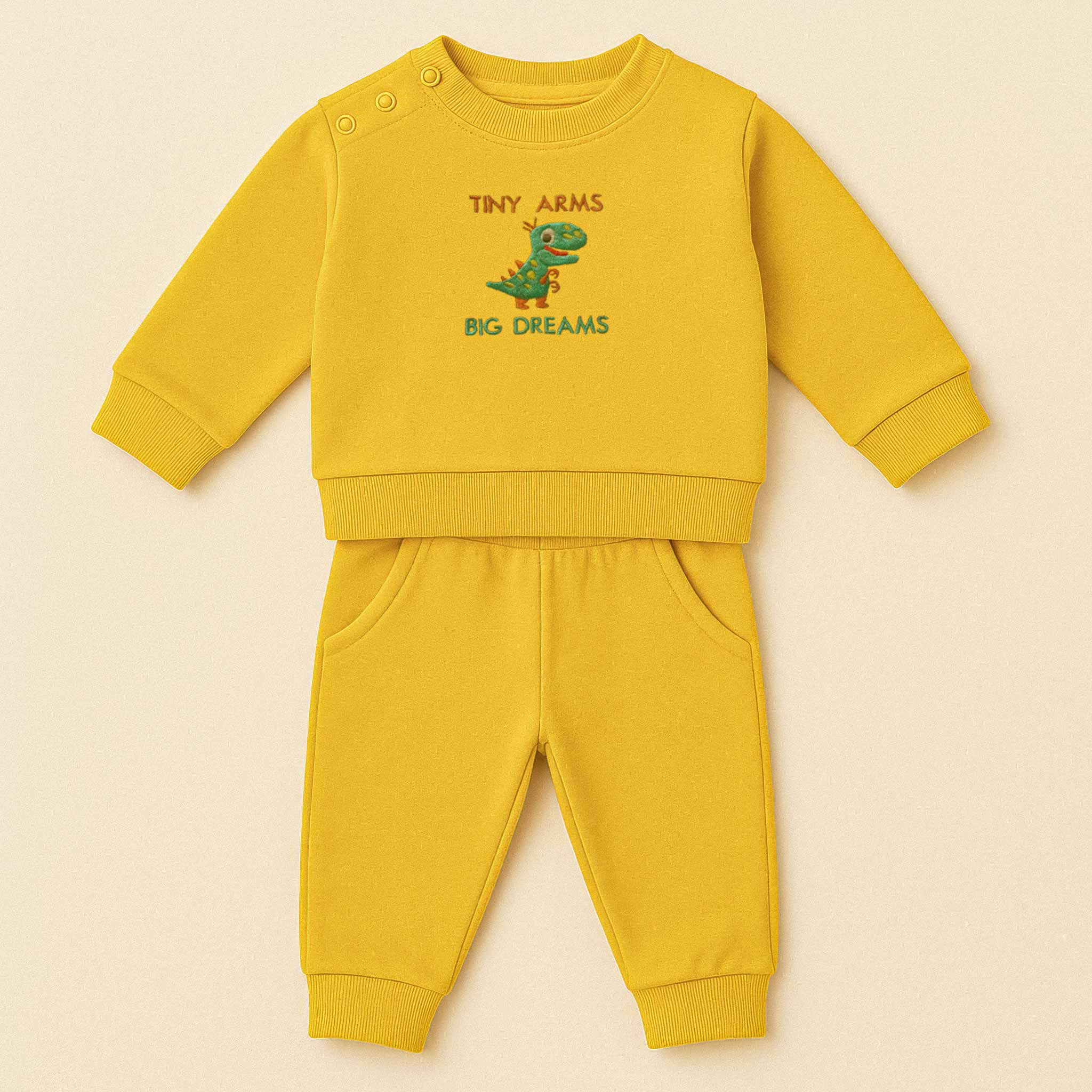 Hardal sarısı renkli, sweatshirt ve pantolondan oluşan, üzerinde sevimli bir T-Rex dinozoru ve "Tiny Arms Big Dreams" baskısı bulunan, omuzdan çıtçıtlı pamuklu bebek eşofman takımı.