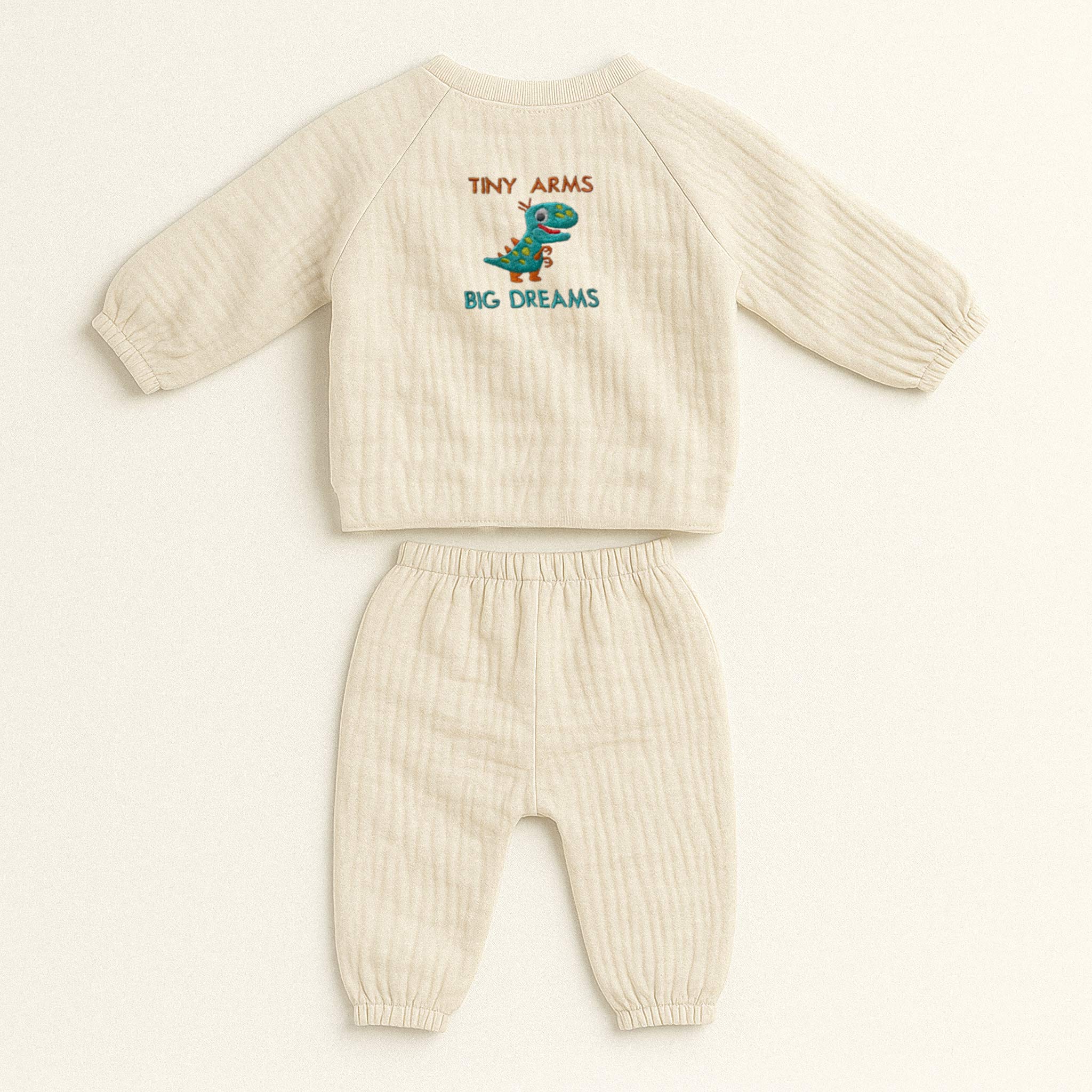 Doğal ekru (bej) renginde, müslin kumaştan yapılmış, üzerinde sevimli bir T-Rex dinozoru ve "Tiny Arms Big Dreams" baskısı bulunan, yandan bağlamalı kimono üst ve pantolondan oluşan yenidoğan bebek takımı.