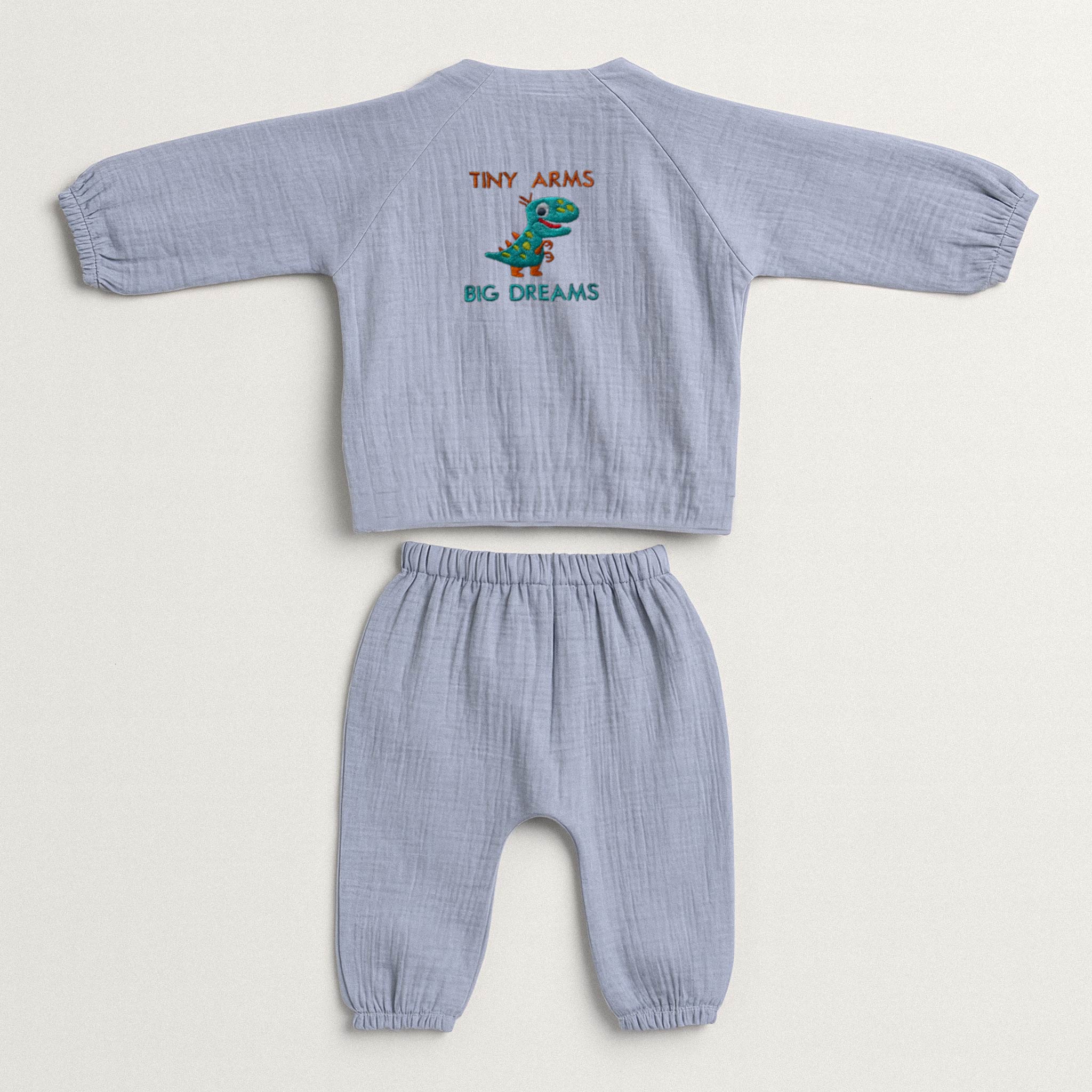 İndigo mavisi renginde, müslin kumaştan yapılmış, üzerinde sevimli bir T-Rex dinozoru ve "Tiny Arms Big Dreams" baskısı bulunan, yandan bağlamalı kimono üst ve pantolondan oluşan yenidoğan bebek takımı.