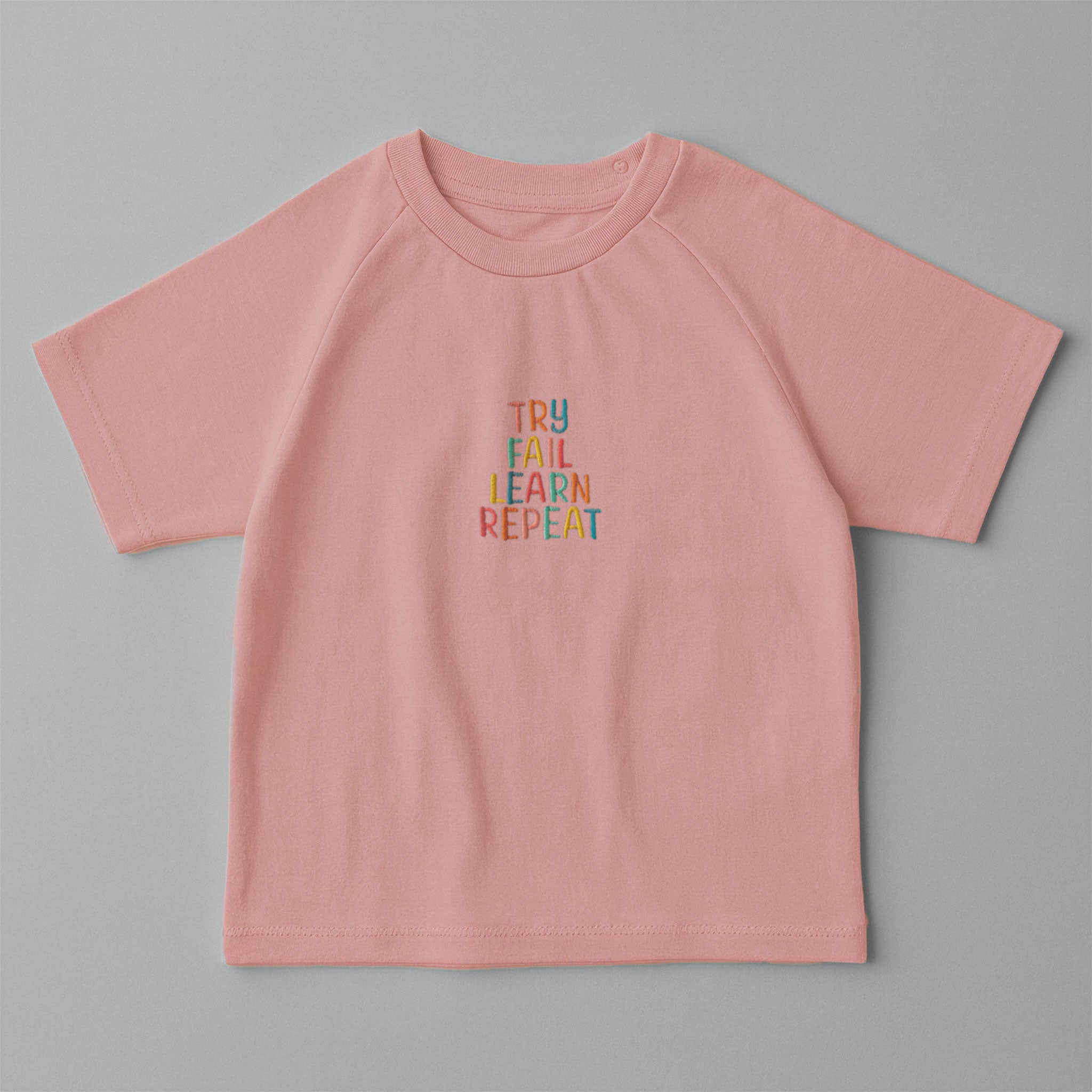 Gül kurusu (pembe) renkli, reglan kollu, omuzdan çıtçıtlı bebek tişörtü. Göğüs kısmında renkli ipliklerle "TRY FAIL LEARN REPEAT" yazısı işlenmiştir.