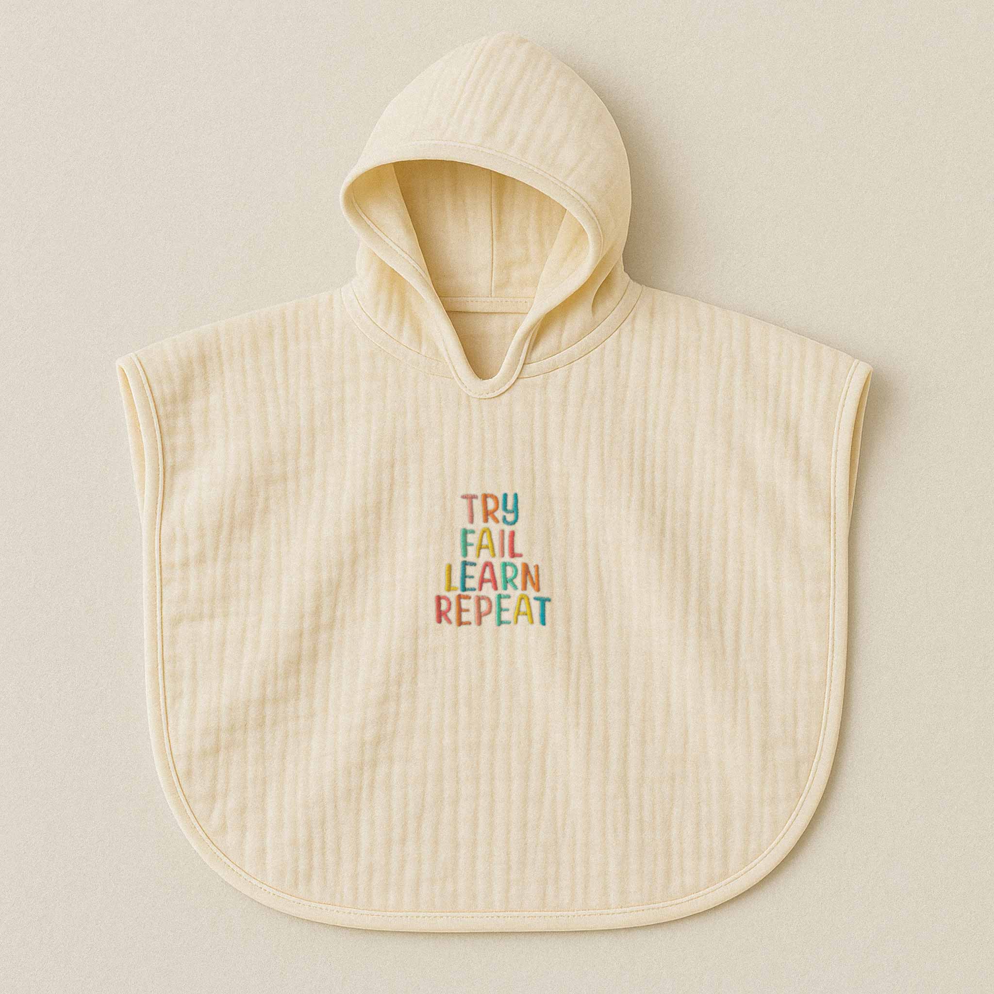 Ekru (doğal bej) renginde, kapüşonlu, müslin kumaştan bebek ve çocuk pançosu. Göğüs kısmında renkli ipliklerle "TRY FAIL LEARN REPEAT" yazısı işlenmiştir.
