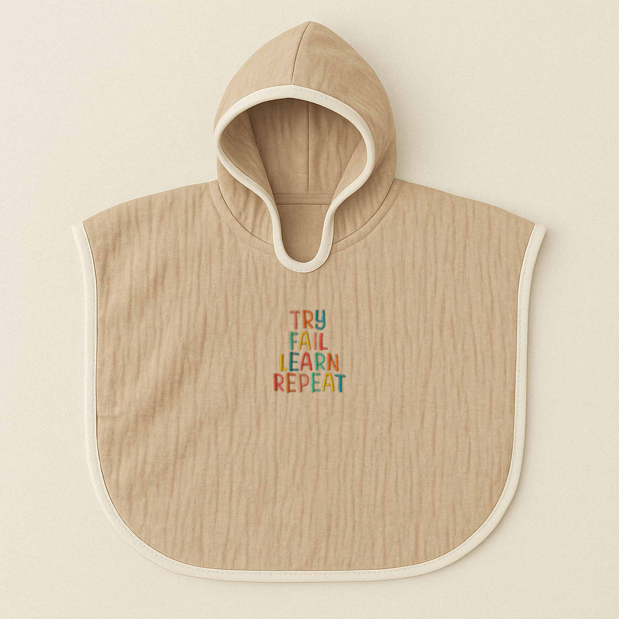 Somon rengi (bej), kapüşonlu, müslin kumaştan bebek ve çocuk pançosu. Göğüs kısmında renkli ipliklerle "TRY FAIL LEARN REPEAT" yazısı işlenmiştir.