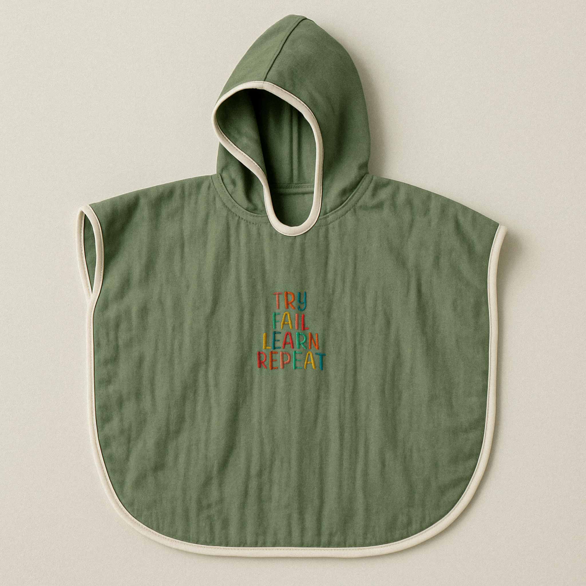 Haki yeşili renginde, kapüşonlu, müslin kumaştan bebek ve çocuk pançosu. Göğüs kısmında renkli ipliklerle "TRY FAIL LEARN REPEAT" yazısı işlenmiştir.