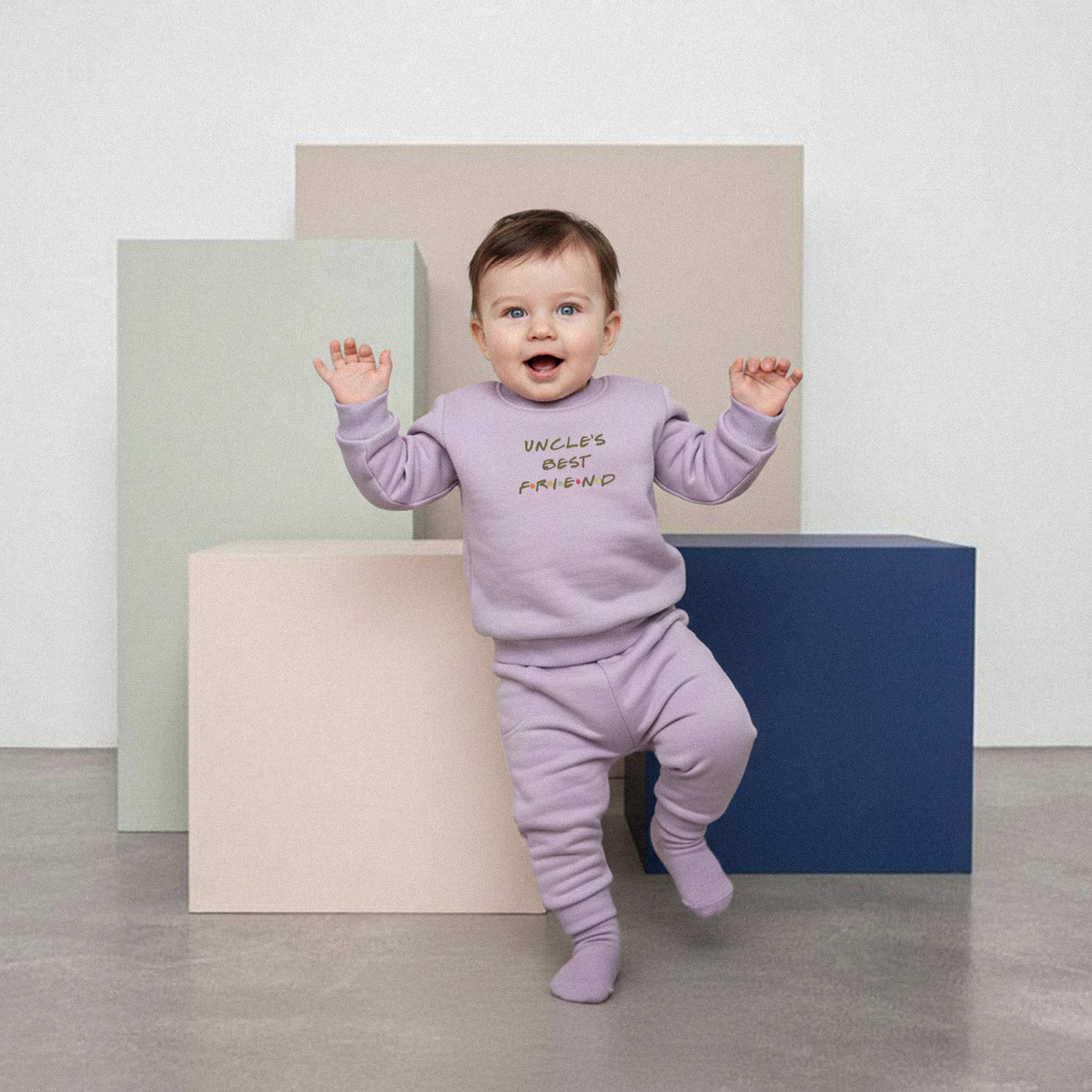 Üzerinde lila renkli, 'Uncle's Best Friend' nakışlı eşofman takımı bulunan sevimli bebek, renkli küplerin önünde yürümeye çalışırken neşeyle ellerini kaldırıyor.