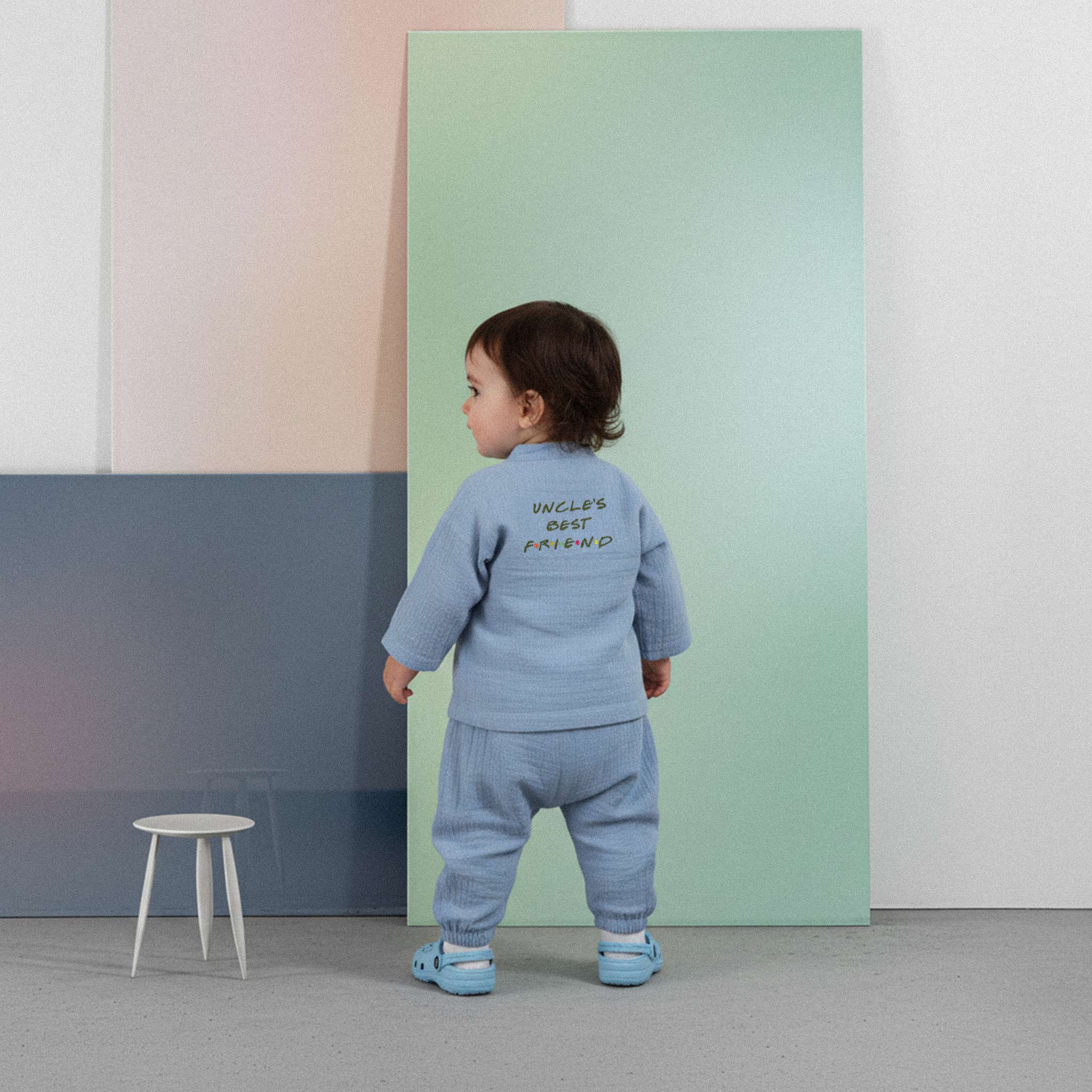 Üzerinde indigo mavisi renkli, 'Uncle's Best Friend' baskılı müslin kimono takımı bulunan sevimli bebek, renkli küplerin önünde ayakta durarak poz veriyor.