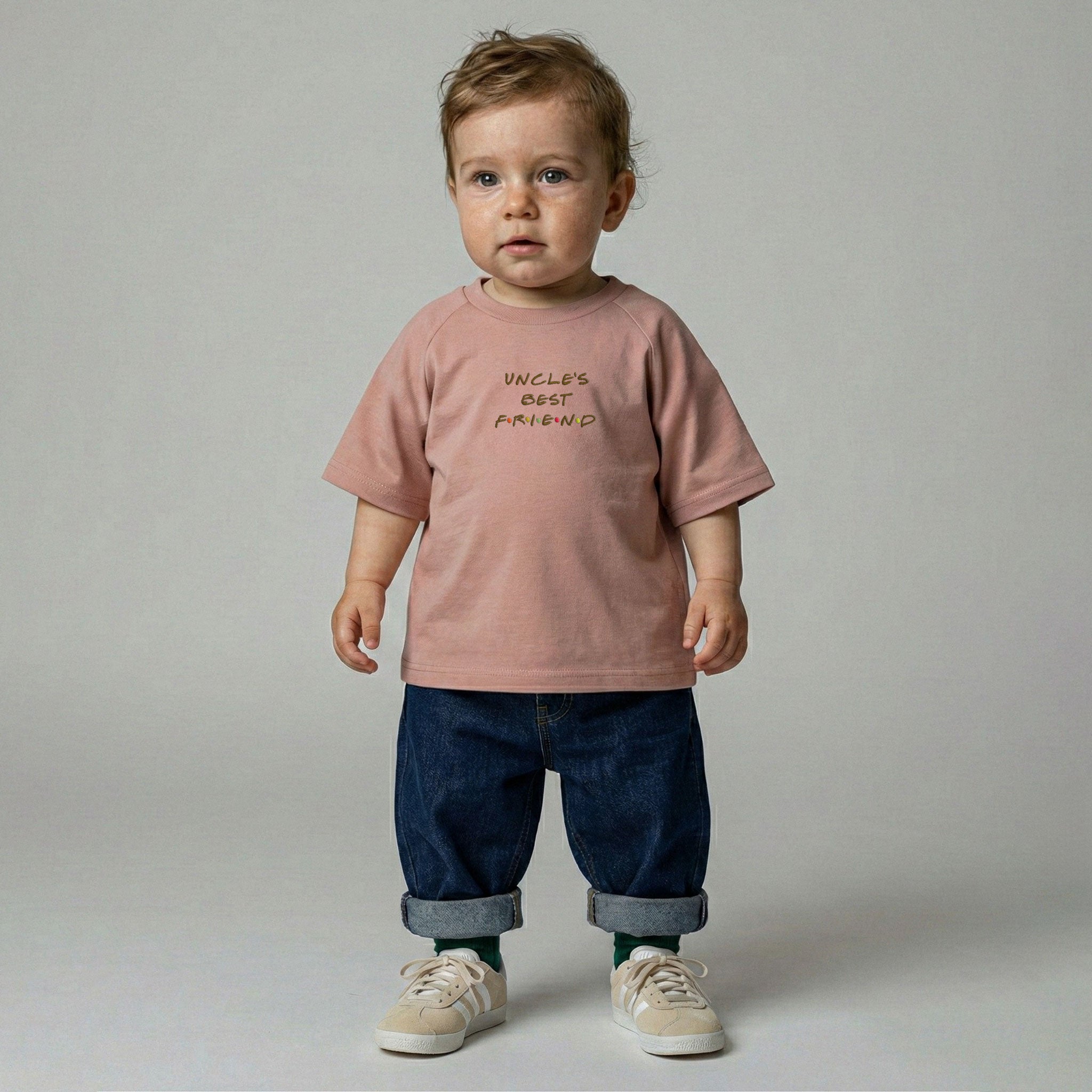 Gül kurusu renginde 'Uncle's Best Friend' nakışlı tişört ve katlanmış paçalı bol jean giyerek ayakta duran erkek bebek model.
