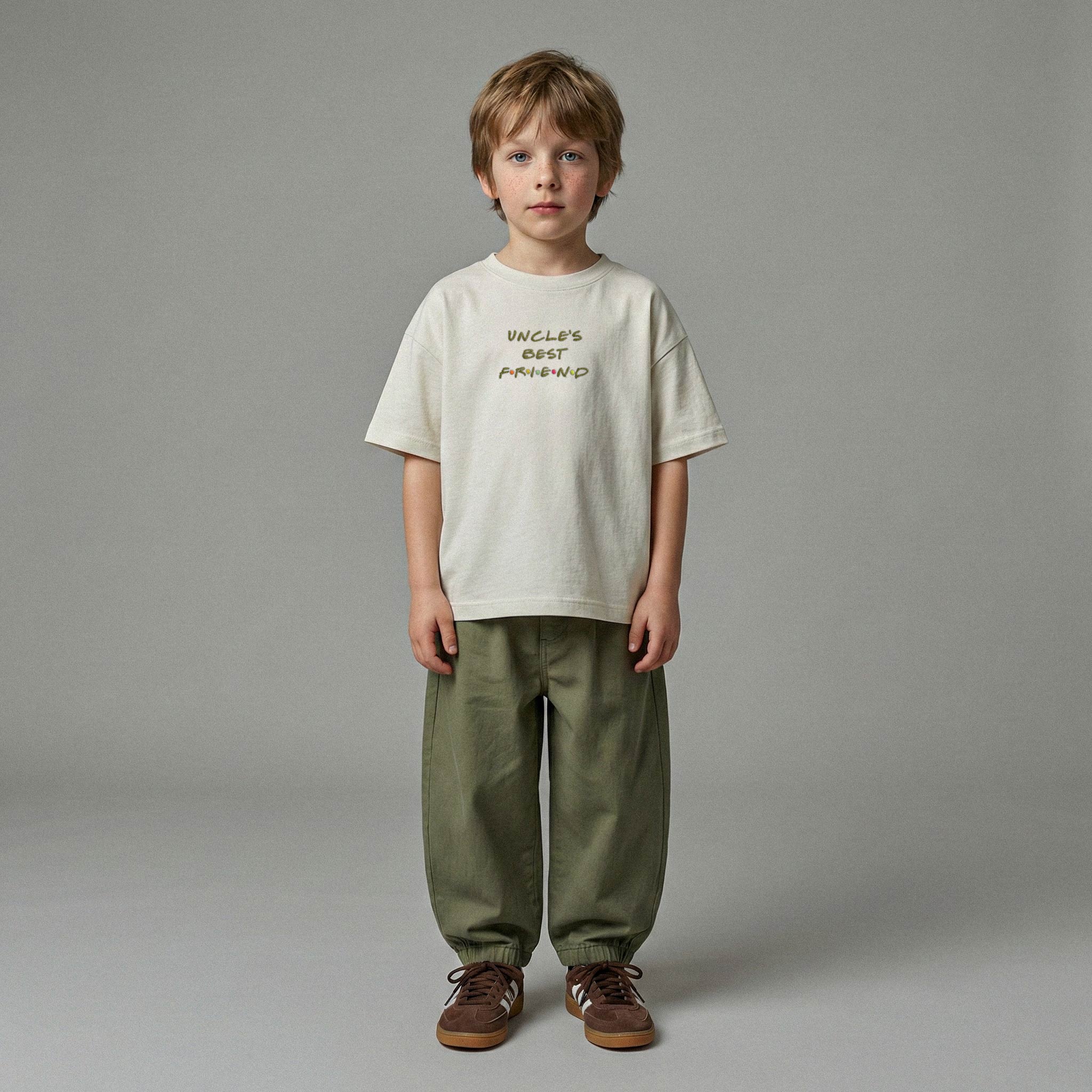Ekru renkli, 'Uncle's Best Friend' nakışlı oversize tişört ve haki yeşili bol pantolon giyen erkek çocuk model.