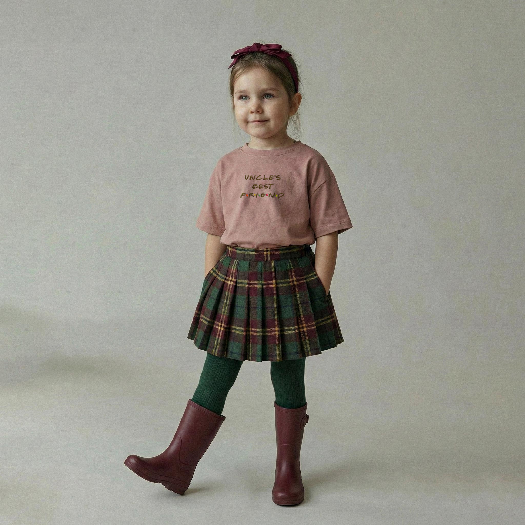 Gül kurusu renginde 'Uncle's Best Friend' nakışlı oversize tişört, ekose etek ve bordo yağmur çizmesi giyen kız çocuk model.