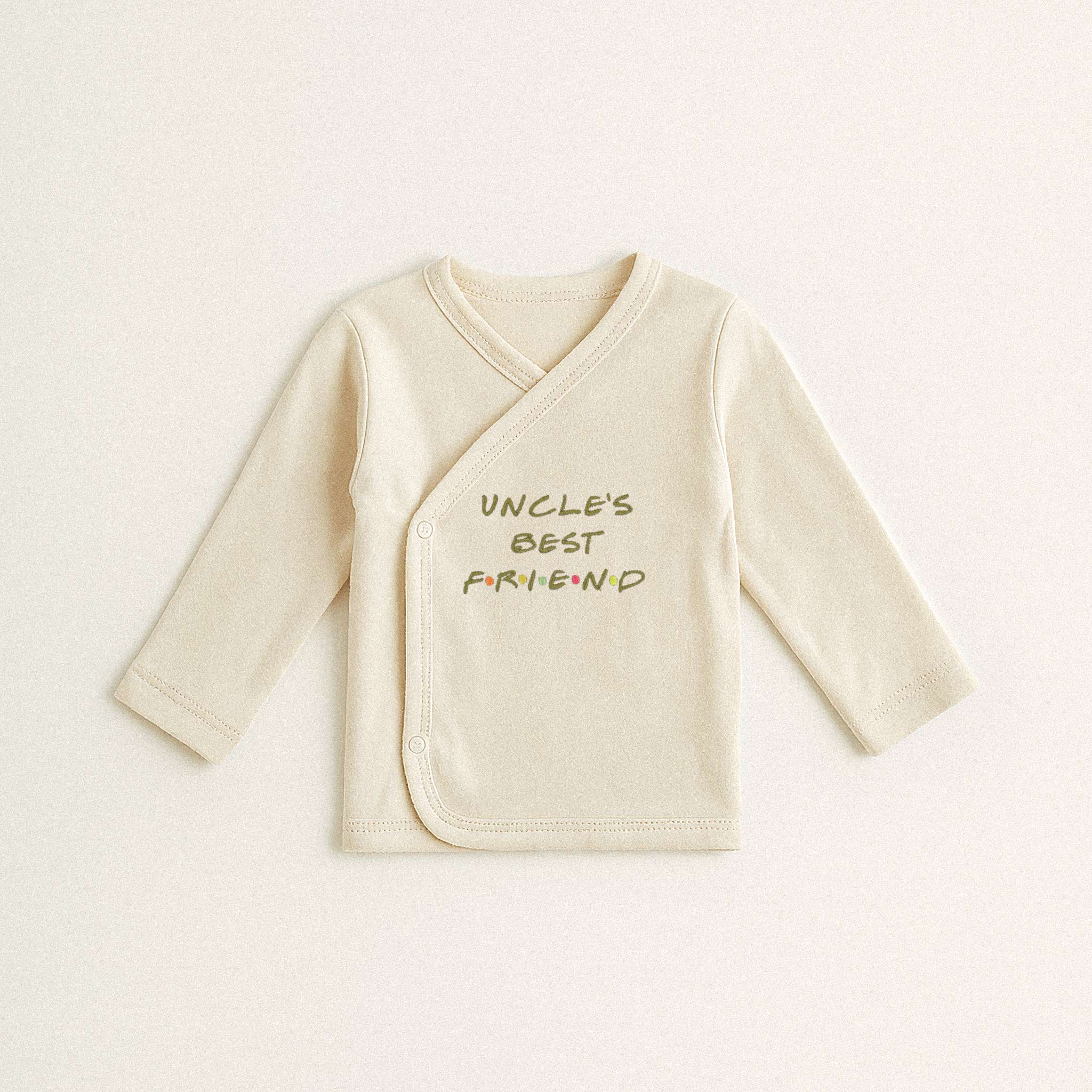 Beyaz arka plan üzerinde duran, ekru renkli, %100 pamuklu, uzun kollu kruvaze yenidoğan üst. Üzerinde Friends dizisi stilinde renkli harflerle "UNCLE'S BEST FRIEND" yazısı bulunmaktadır.