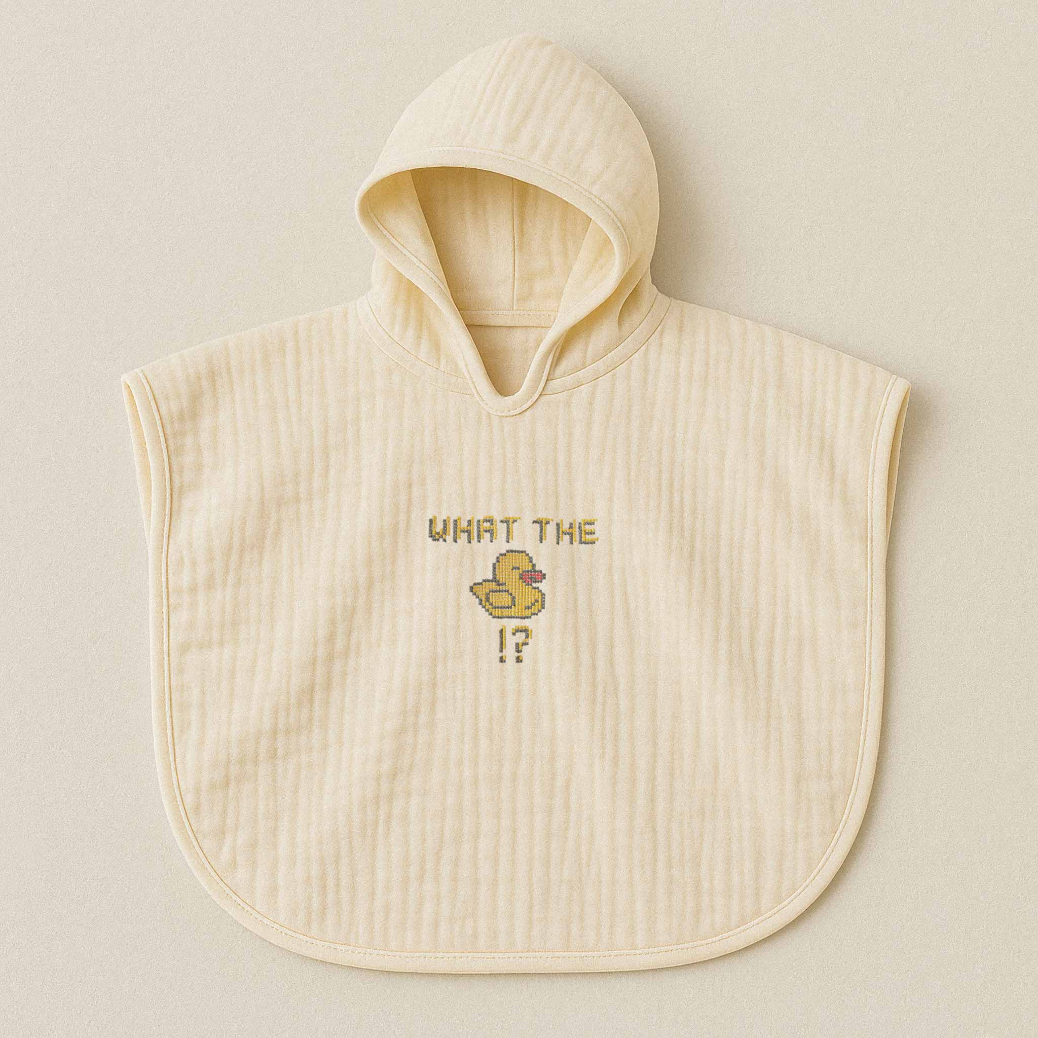 Ekru (doğal bej) renginde, kapüşonlu, müslin kumaştan bebek ve çocuk pançosu. Göğüs kısmında "WHAT THE" yazısı, bir ördek figürü ve soru işareti nakışla işlenmiştir.