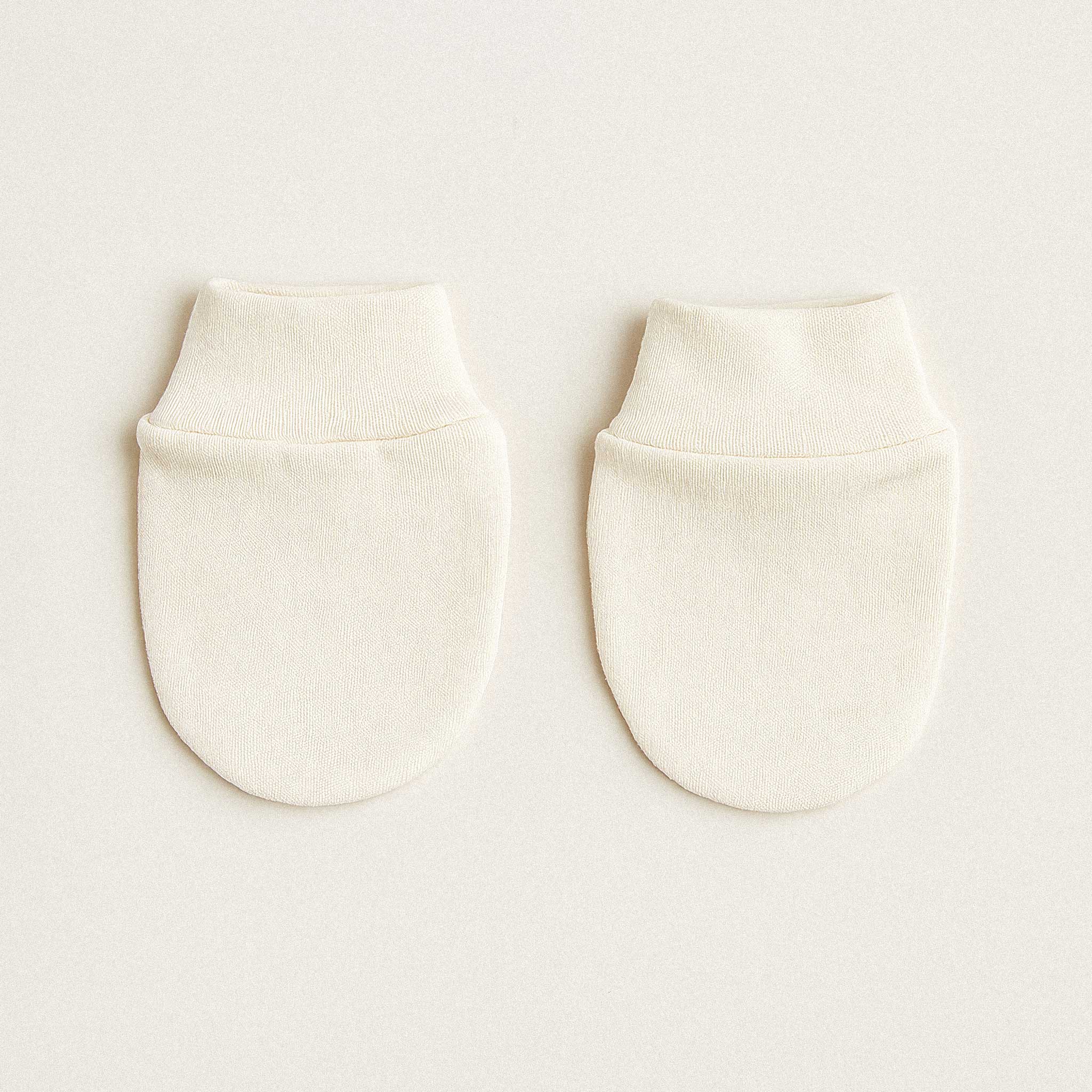 Bir çift ekru renkli, %100 pamuklu, çizilmeyi önleyici yenidoğan bebek eldiveni.